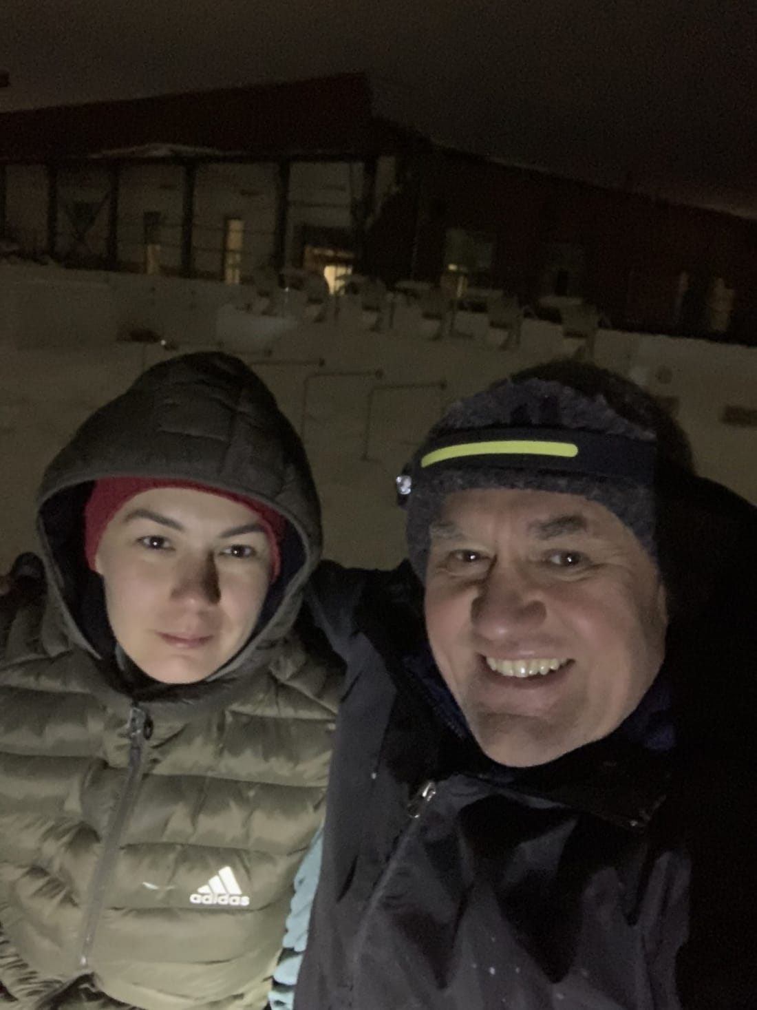 Two people in winter jackets on a site at night