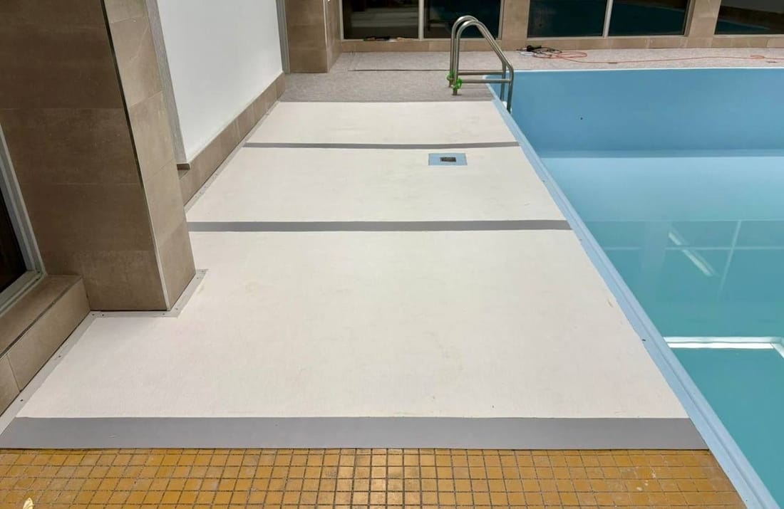 A pool deck covered in light PVC membrane beside the water