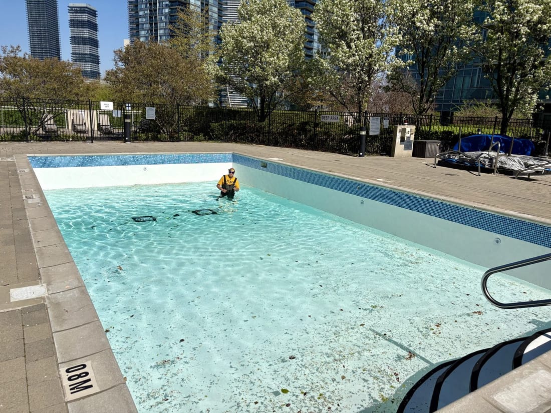 A pool being lined in light membrane, a worker in it, city buildings behind