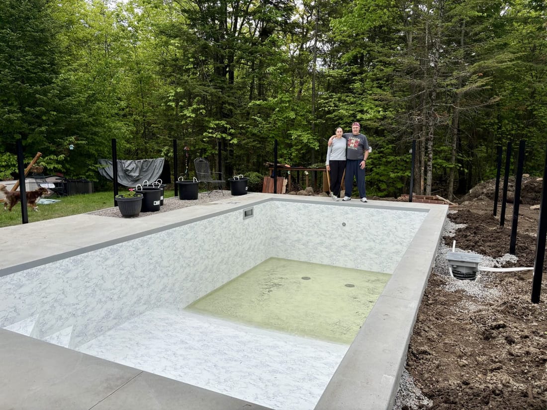 A backyard pool newly lined in white marble-pattern membrane, a little water in the deep end, two people on the far edge