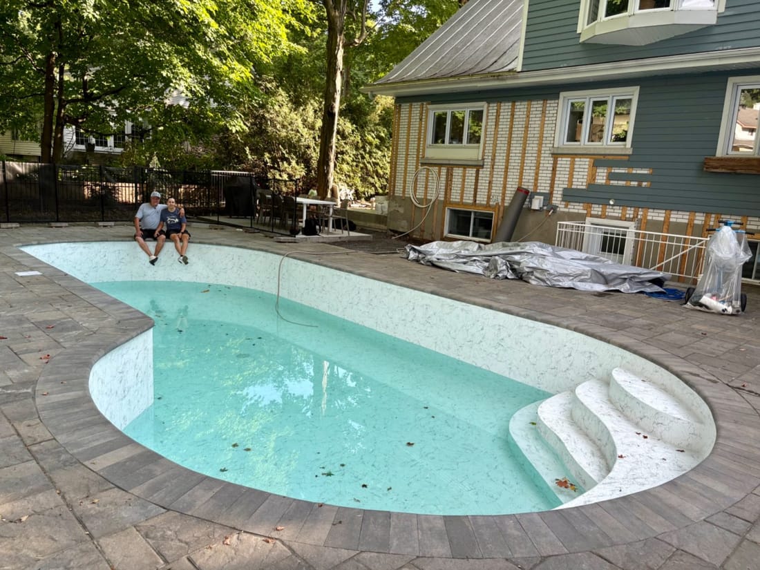 A backyard pool in white marble-pattern membrane filling with water, curved steps and a house behind it