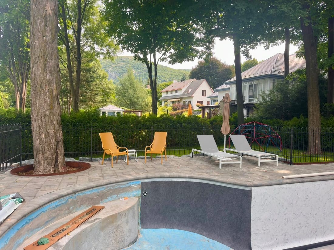 A curved backyard pool during relining, dark underlay on the wall, loungers on the stone deck