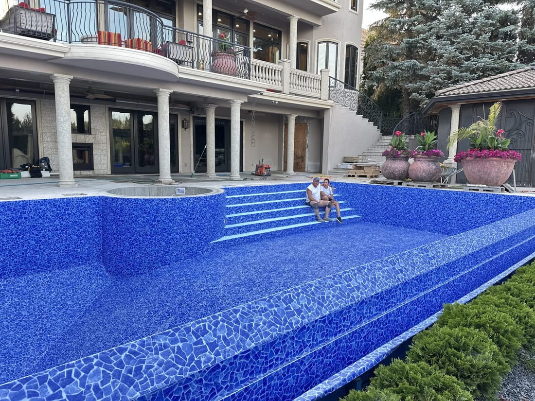 A large pool in blue mosaic membrane with wide steps, in front of a house with columns