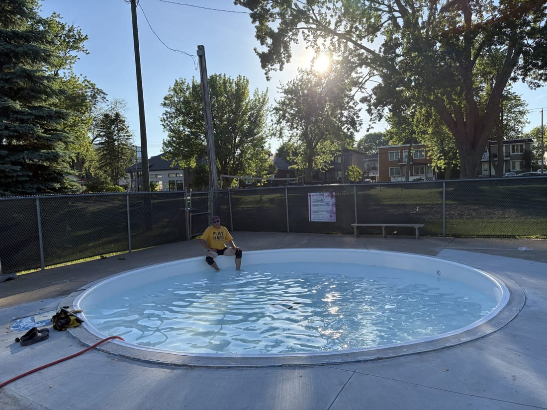 The same round pool re-lined in pale membrane and full of water, one person sitting on its edge