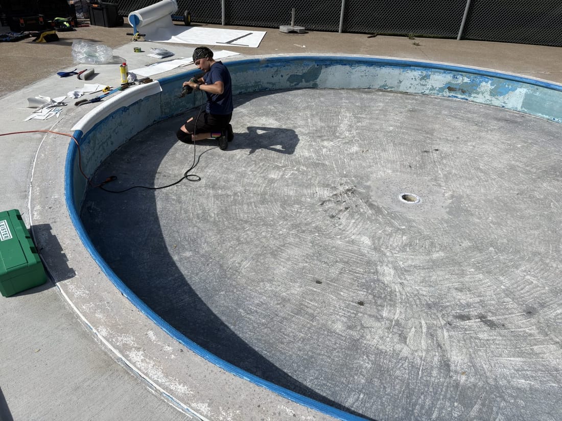 The old dark surface of a round public pool, with the membrane work beginning