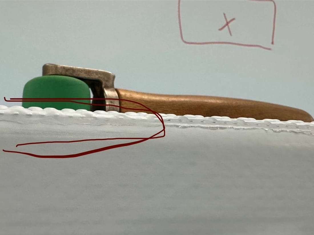 Close-up of the welded edge of a white membrane with a seam roller resting on it and red marker lines drawn around the seam