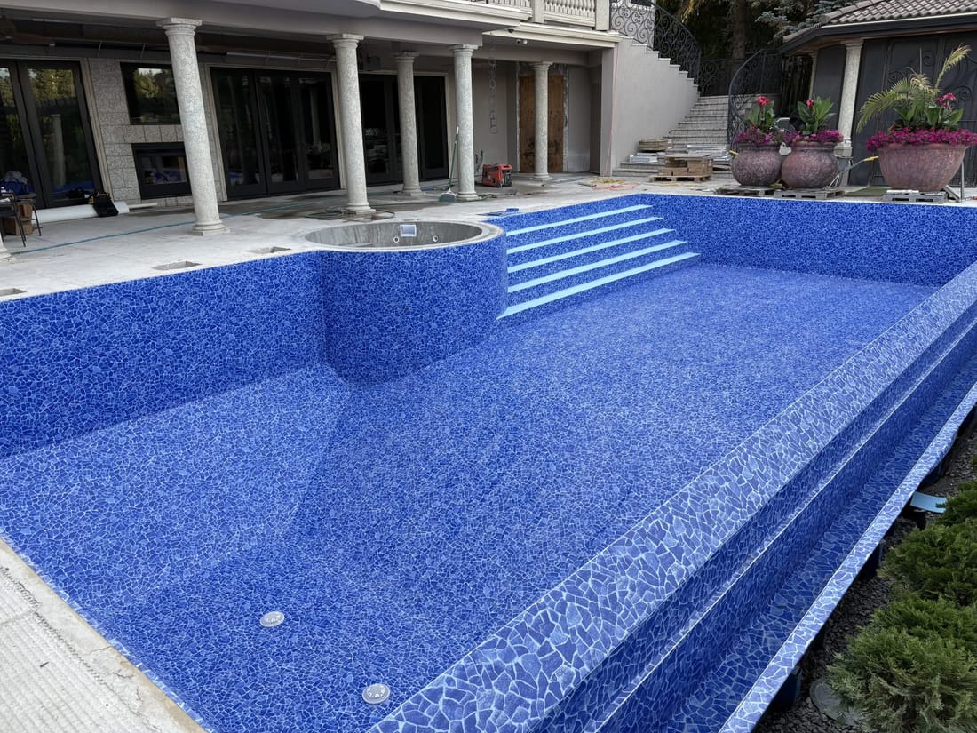 A backyard pool with corner steps, lined in blue mosaic membrane