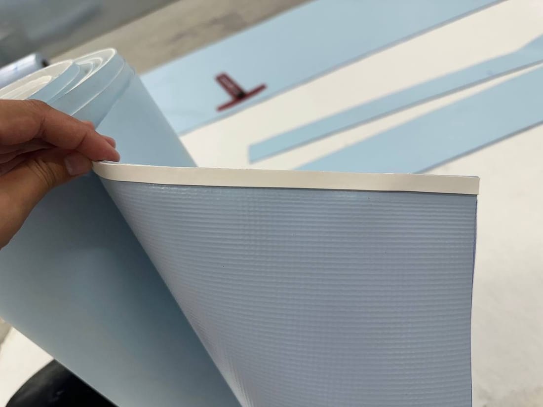 A hand lifting reinforced PVC membrane, the reinforcing mesh visible inside it