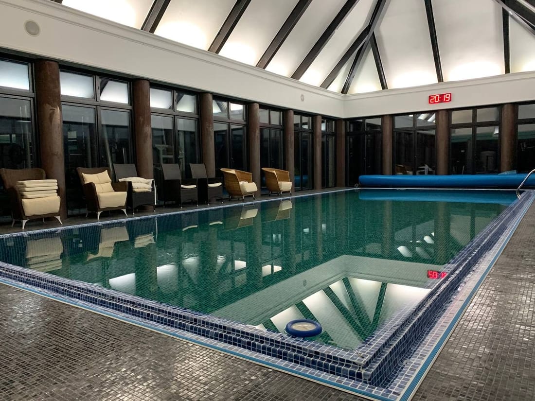 An indoor pool under a glazed roof with loungers along one side